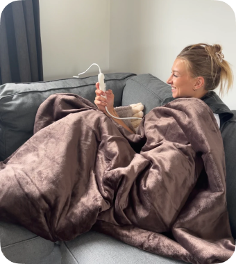 Vrouw bedient haar Seranova warmtedeken met afstandsbediening – ontspannen moment op de bank
