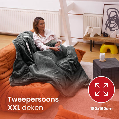 Vrouw onder een tweepersoons XXL elektrische warmtedeken van 180x160cm – ideaal voor samen ontspannen op de bank.