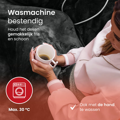 Vrouw met kopje thee onder een wasmachinebestendige elektrische warmtedeken – eenvoudig te reinigen tot 30 °C.