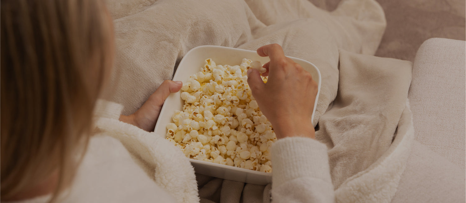 Vrouw onder warme fleece elektrische deken met popcorn – ideaal voor filmavonden thuis. 